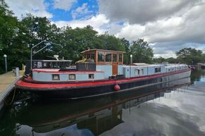 Vintage 1926 Dutch Barge Luxemotor moored on a calm river under a cloudy sky.