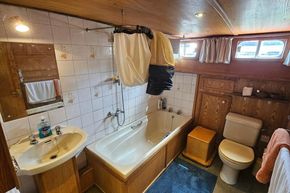 Luxemotor Dutch Barge 1926 bathroom with wooden interior, bathtub, sink, and toilet.