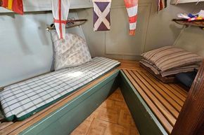 Cozy cabin interior of a 1927 Classic Dutch Barge with nautical flags and cushions.
