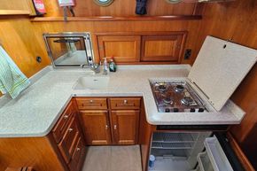 Compact kitchen in a 2005 Stevens 1200 Vlet boat with stove, sink, and wooden cabinetry.