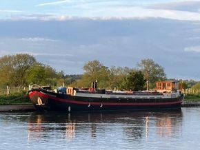 Classic 1901 Dutch Barge moored on a tranquil river with lush greenery.