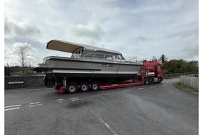 2025 Linssen 45 SL Sedan yacht on trailer, transported by red truck under cloudy sky.