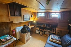 Cozy interior of a 1926 Dutch Barge Luxemotor with wooden paneling and storage shelves.