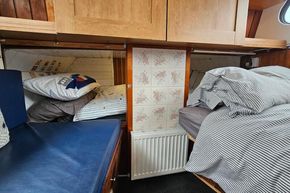 Cozy cabin interior of a 1921 Classic Dutch Barge with wooden cabinets and striped bedding.