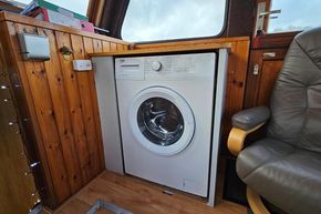 Washing machine inside a 1921 Classic Dutch Barge with wooden interior and leather chair.