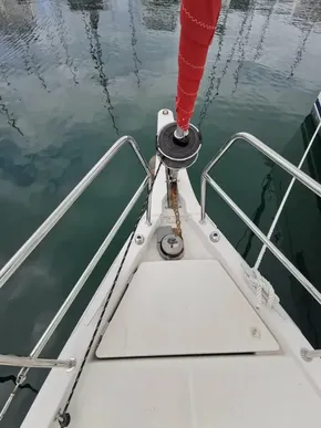 Bow of 2020 Jeanneau Sun Odyssey 410 sailboat with red sail, docked on calm water.