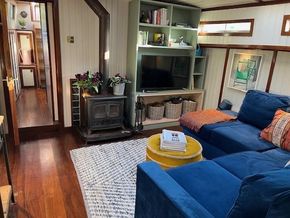 Cozy interior of a 1901 Classic Dutch Barge with blue sofa, wood stove, and TV.