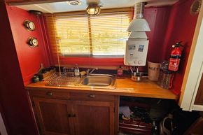 1927 Classic Dutch Barge kitchen with red walls, wooden cabinets, and a small sink.