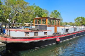 Luxemotor Dutch barge from 1926 docked on a sunny day, surrounded by greenery.