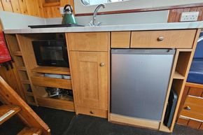 Compact kitchen area in a 1921 Classic Dutch Barge with wooden cabinetry and modern appliances.