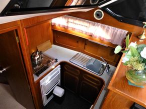 Compact kitchen in 1995 Aquafibre Bounty Boats 10/70, featuring stove, sink, and wooden cabinetry.