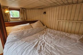 Cozy bedroom inside a 1926 Dutch Barge Luxemotor with wooden walls and soft bedding.