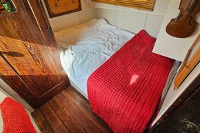 Cozy bedroom in a 1927 Classic Dutch Barge with red quilt and wooden decor.