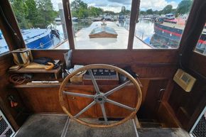 Wheelhouse of a 1926 Dutch Barge Luxemotor, featuring a wooden steering wheel and river view.