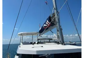 Sailing catamaran Leopard 42, 2022 model, with mast and flags against clear blue sky.