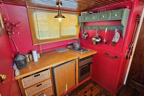 Cozy 1927 Classic Dutch Barge kitchen with red walls, wooden countertop, and hanging utensils.