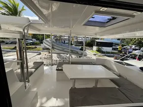 Spacious interior of 2019 Leopard 40 catamaran with seating and table, docked near palm trees.