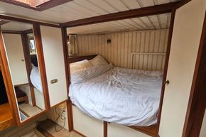 Cozy bedroom inside a 1926 Dutch Barge Luxemotor, featuring wood paneling and a comfortable bed.