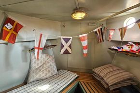 Interior of a 1927 Classic Dutch Barge with nautical flags and cozy bedding.