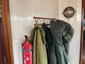 Coats hanging on hooks inside a 1901 Classic Dutch Barge, with a fire extinguisher nearby.