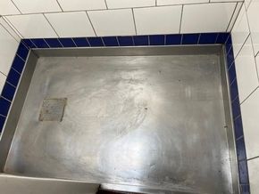 Stainless steel shower tray with blue and white tiled edges, featuring a square drain.