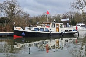 Classic 1921 Dutch Barge moored on a calm river, surrounded by trees and boats.