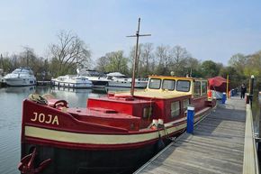 Classic 1927 Dutch Barge moored at a scenic marina with surrounding boats.