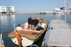 People enjoying a ride on a 2026 Enkhuizensloep 780 boat at a sunny marina.