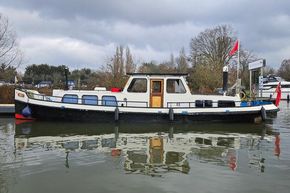 Classic 1921 Dutch Barge on calm water, featuring a white and black exterior with wooden accents.
