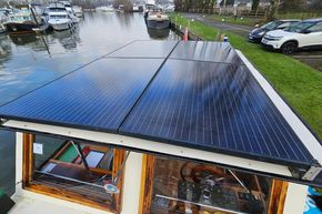 Classic 1921 Dutch Barge with solar panels on roof, docked by a river.