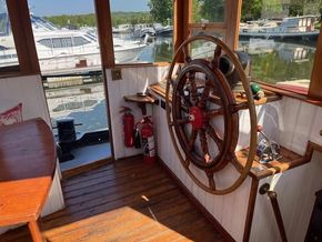 Wheelhouse of a 1901 Classic Dutch Barge with wooden steering wheel and marina view.