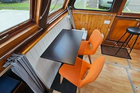 Interior of a 1921 Classic Dutch Barge with orange chairs and wooden accents.
