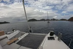 2024 Lagoon 42 catamaran sailing in a scenic bay with cloudy skies.