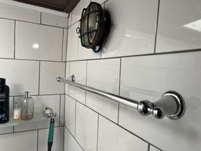 Bathroom with white tiled walls, metal towel bar, and vintage-style light fixture.