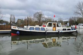 Classic 1921 Dutch Barge on calm water, featuring a traditional design and vibrant flags.