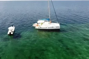 Aerial view of 2008 Leopard 38 catamaran and small boat on clear, green ocean water.