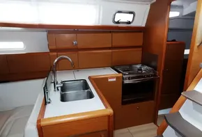 2017 Jeanneau Sun Odyssey 389 galley with sink, stove, and wooden cabinetry.